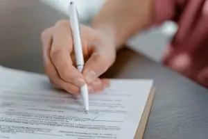 Mano de una persona firmando un documento con un bolígrafo blanco sobre una mesa, simbolizando la firma del contrato de compra de una casa en Barcelona