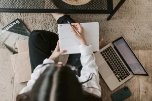 Vista superior de una persona organizando su agenda mientras trabaja en una computadora portátil, representando la importancia de la planificación y gestión efectiva en la administración de apartamentos para estudiantes