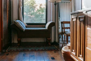 Rincón de lectura junto a una ventana, con un banco acolchado, cojín a rayas y una lámpara de pie, mostrando cómo crear un espacio acogedor para relajarse y leer en un área pequeña