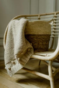 Wicker basket with a knitted blanket over a rattan chair, showing how to use natural textures to create a cozy and warm atmosphere in home decor.