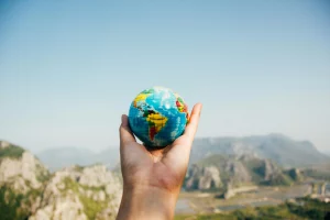 Una mano sosteniendo un globo terráqueo en un paisaje montañoso, representando el impacto global del turismo responsable y la importancia de viajar de manera consciente para proteger el planeta