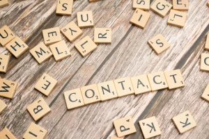 Palabras formadas con piezas de juego de letras en una mesa de madera, destacando la palabra "CONTACT", simbolizando la importancia de la comunicación en el sector turístico