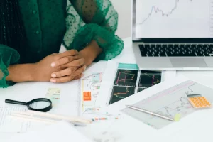 Close-up of a person in front of financial charts, a laptop, and a magnifying glass, symbolizing the process of investment analysis and strategic financial decision-making.