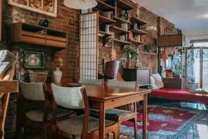 Living room with eclectic decor, combining wooden furniture, open shelves, and an exposed brick wall, showing how to mix different styles and elements to create a unique and personalized home environment.