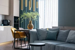 Modern living room with a gray sofa, yellow dining chairs, and a table with a brown glass vase with plants, showing how to combine elegance and functionality in a flat's decoration on a budget.