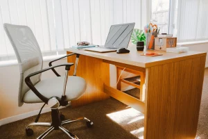 Vista de un escritorio marrón con un ordenador portátil encima, acompañado de una silla ergonómica blanca con ruedas.