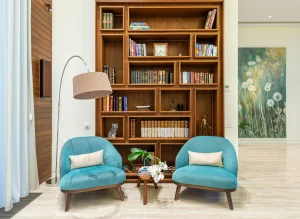 Rincón de lectura con dos sillones turquesa, lámpara de pie y una estantería de madera repleta de libros y adornos.