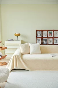 Sofá beige con manta y cojines, mesa auxiliar y revistas de diseño en un ambiente acogedor.