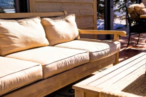 Sofá de madera con cojines beige en una terraza soleada, acompañado de una mesa baja, ideal para descansar al aire libre en un entorno natural.