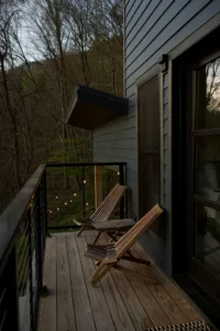 Pequeña terraza de madera con dos sillas plegables frente a un bosque, ideal para desconectar y disfrutar del entorno natural al atardecer.