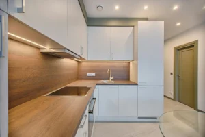 Contemporary kitchen with white linear design cabinets, wood countertop and wall, induction stove, and integrated LED lighting under cabinets