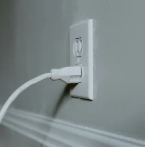 Close-up of a white cable plugged into a wall outlet with white molding and gray wall