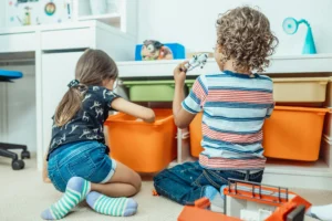 Two small children, seen from behind, organizing colorful toy boxes in a bright, tidy playroom