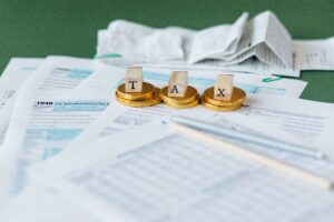 Close-up of U.S. tax forms with golden coins and wooden blocks spelling the word TAX, symbolizing income taxes and financial obligations