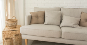 Beige sofa decorated with cushions in cream and brown tones, next to wicker baskets and a white brick wall