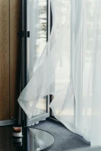 Detail of an open window with sheer curtains softly waving in the breeze, next to a low table with a decorative candle