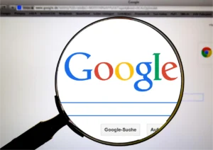 Un primer plano de la página de búsqueda de Google vista a través de una lupa, enfocando el logo de Google colorido y la barra de búsqueda.