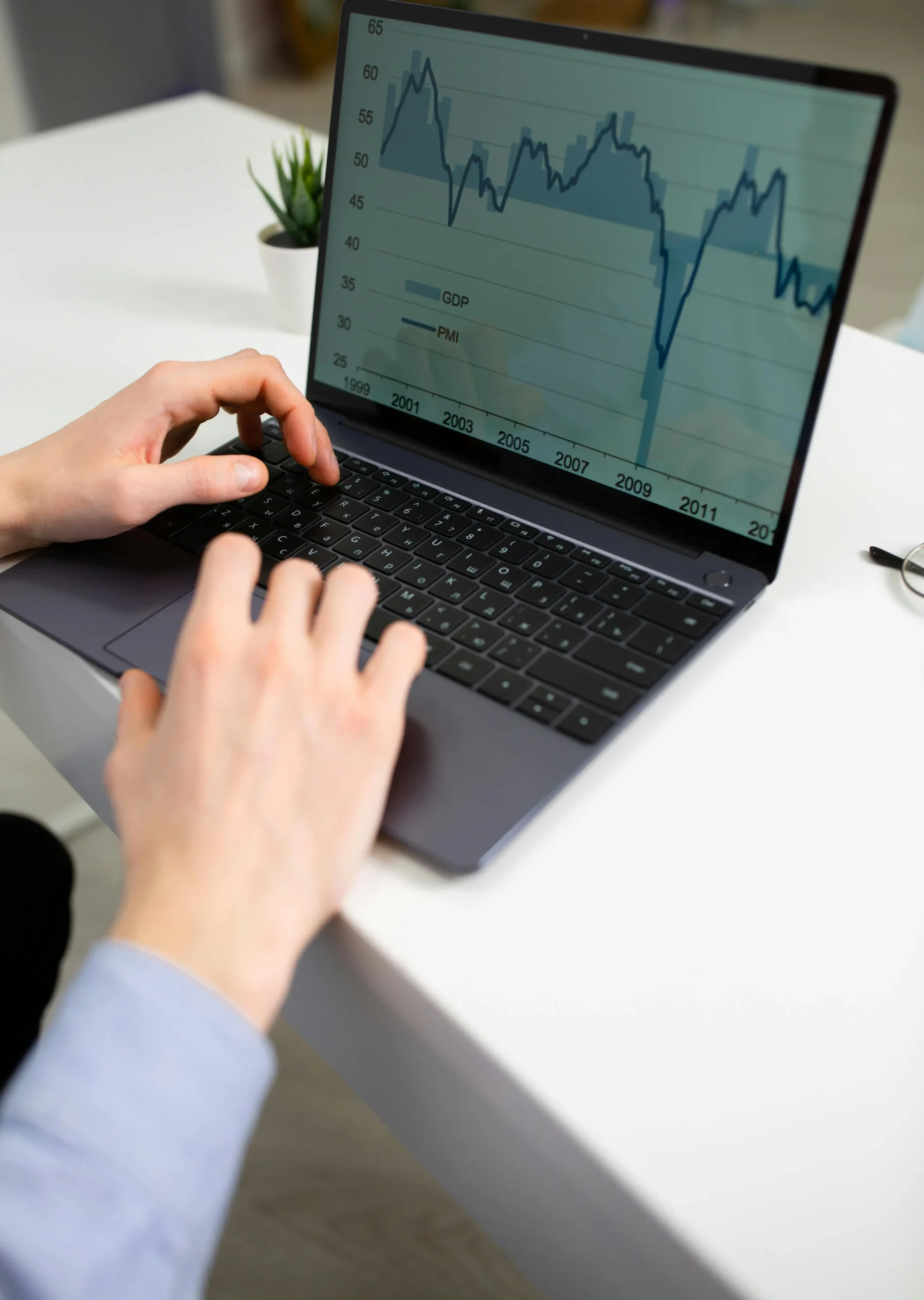 Person analyzing economic data on a laptop with GDP and PMI charts