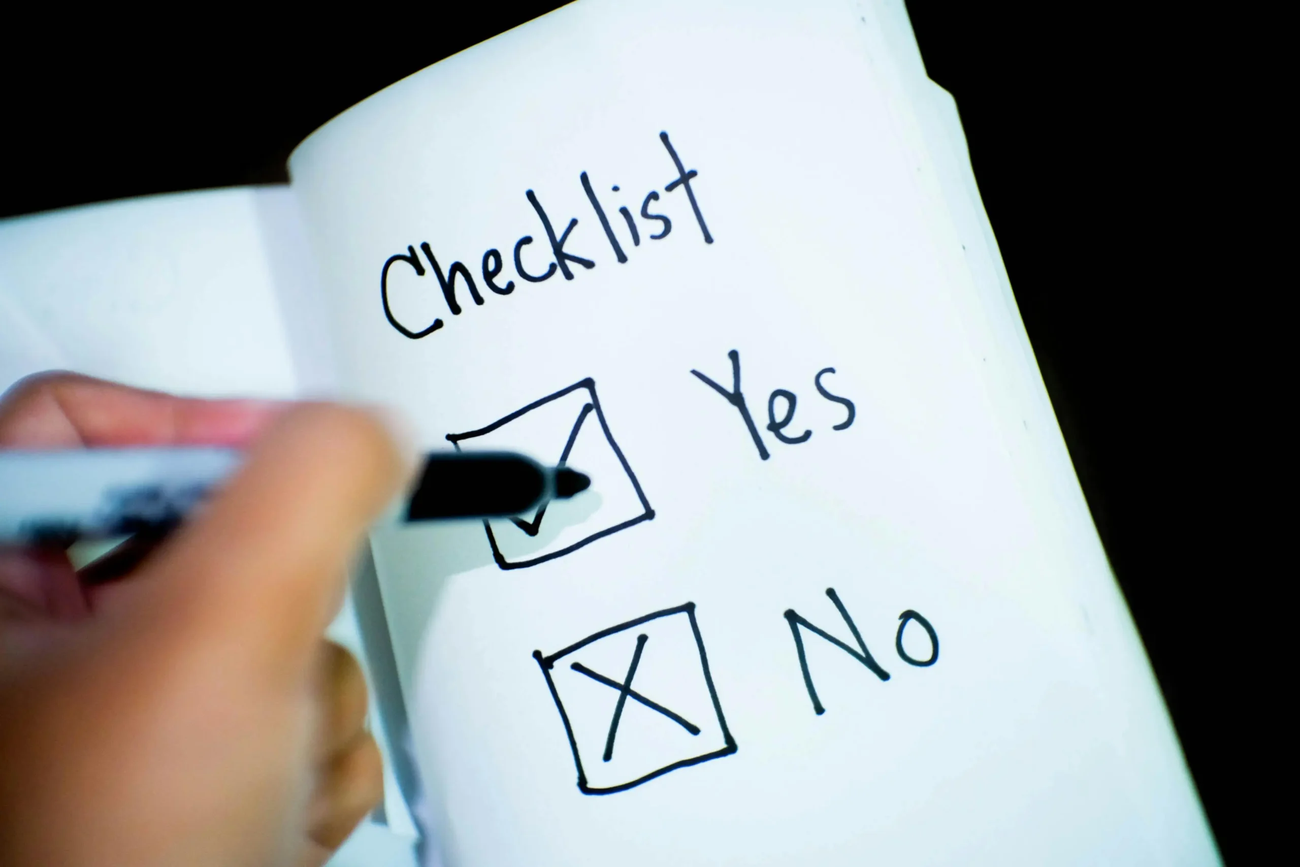Hand checking “Yes” on a handwritten checklist in a notebook