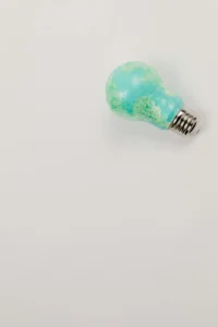 Una bombilla pintada en verde y azul, que representa la Tierra, colocada sobre un fondo blanco, simbolizando creatividad y sostenibilidad.