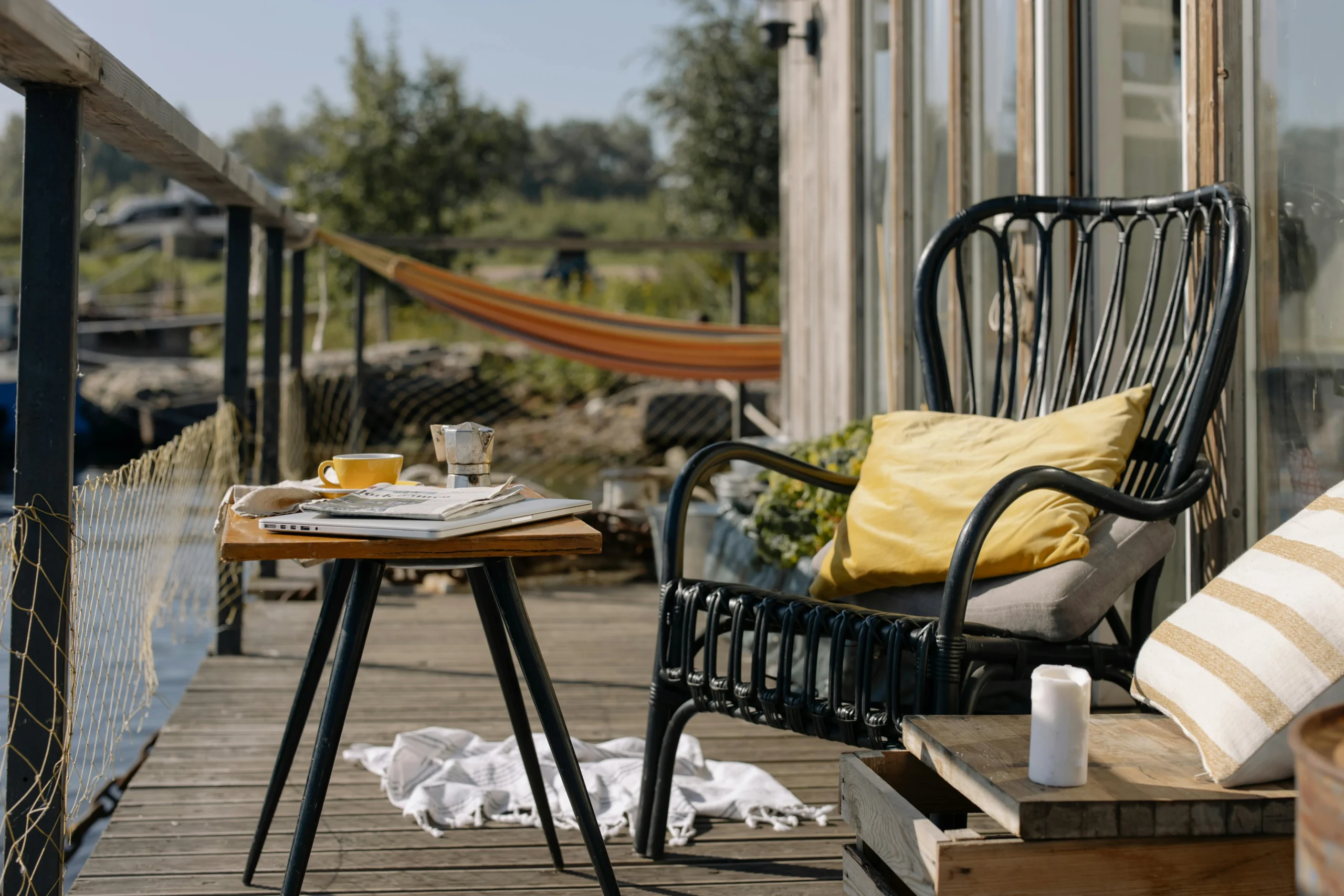 Terraza soleada con sillón de ratán, cojines, mesa con café y hamaca al fondo, evocando un ambiente mediterráneo relajado.