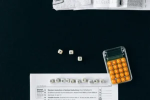Lletres que formen les paraules “TAX” i “DEDUCTIONS” juntament amb una calculadora i documents d'impostos sobre una taula negra