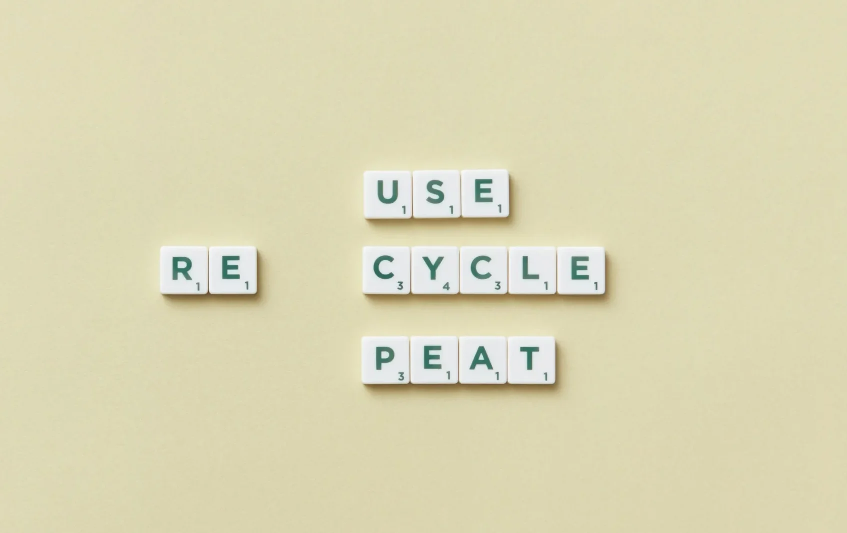 Fichas de Scrabble formando las palabras 'RE', 'USE', 'CYCLE' y 'PEAT' sobre un fondo beige, transmitiendo el mensaje ecológico 'Reuse, Recycle, Repeat'."