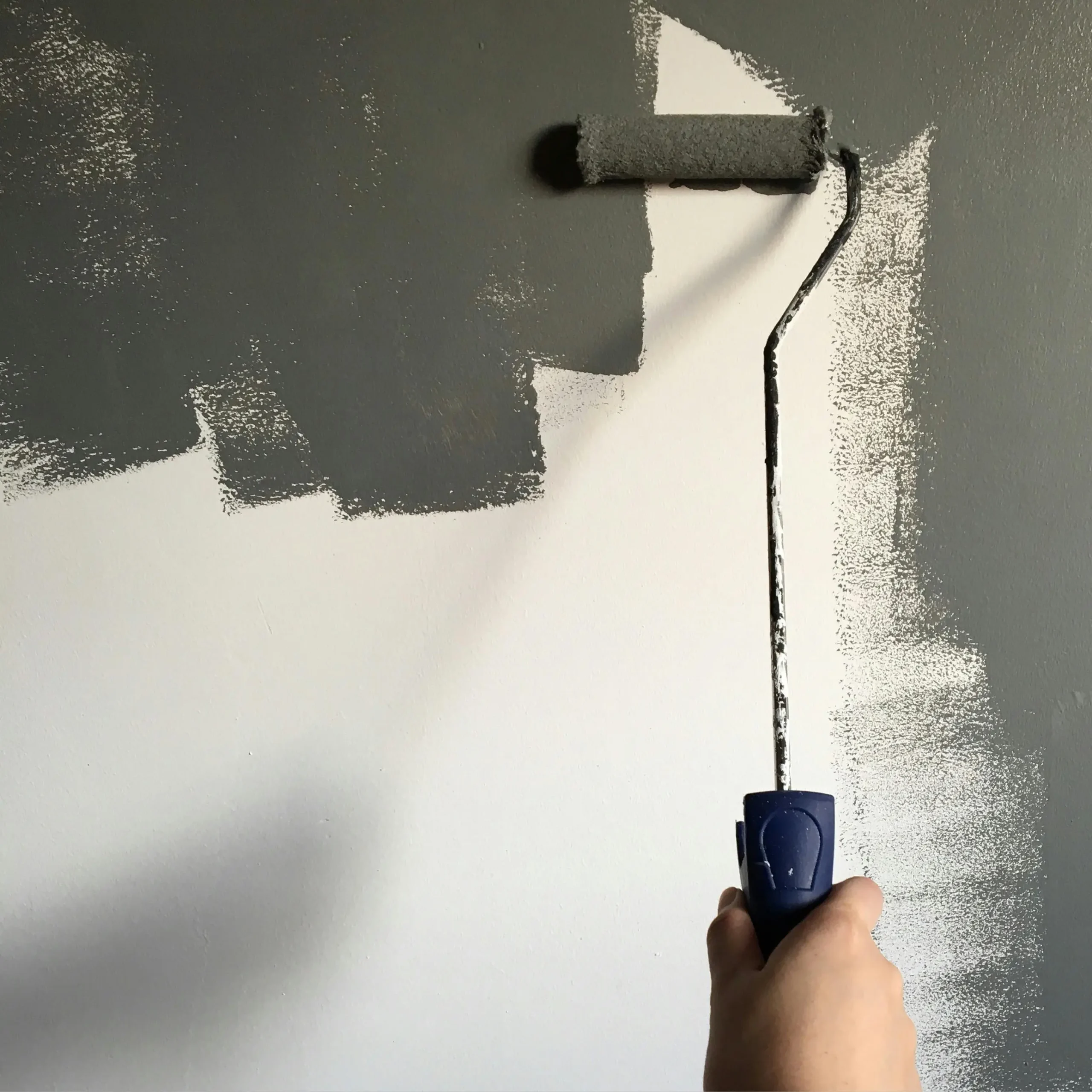 Hand holding a roller while painting a white wall with dark grey paint