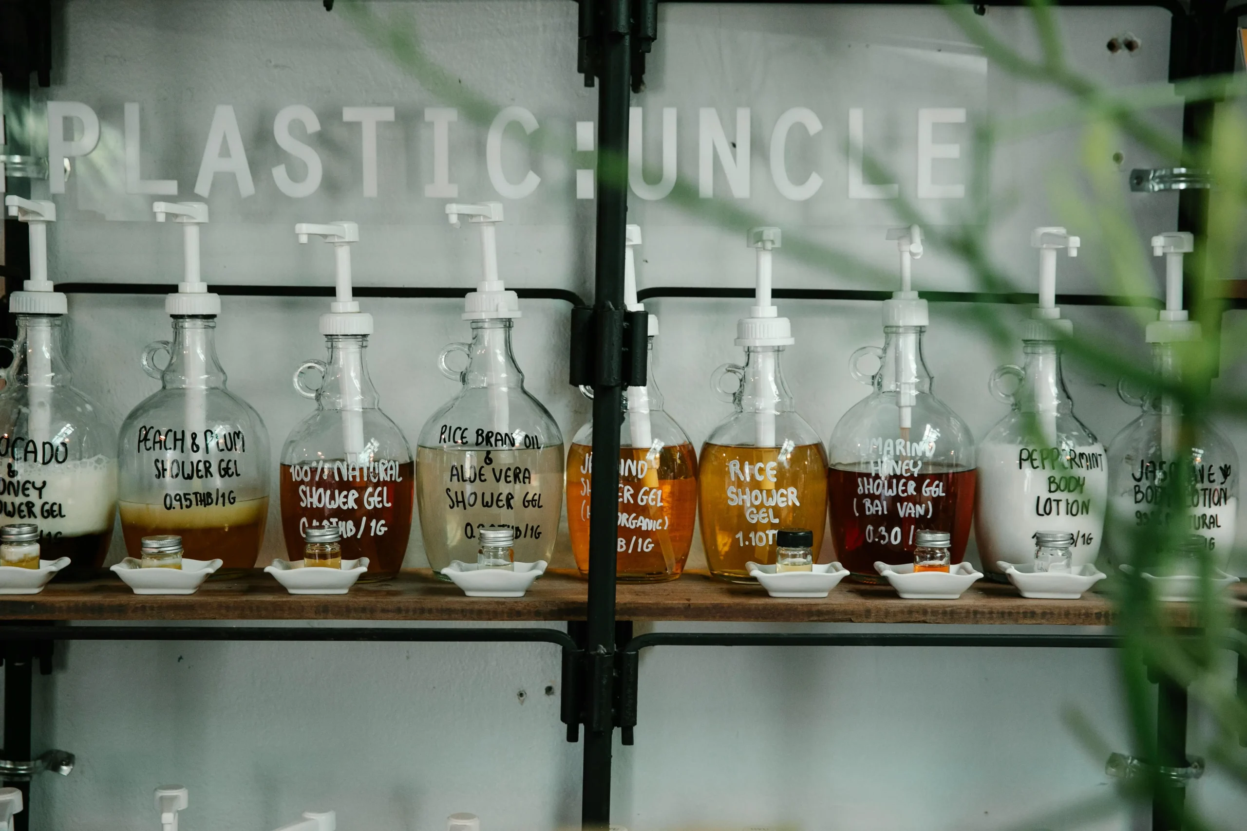 Frascos de vidrio reutilizables con dispensadores blancos alineados en estanterías, conteniendo distintos tipos de gel de ducha y lociones corporales naturales con etiquetas escritas a mano, en una tienda sostenible