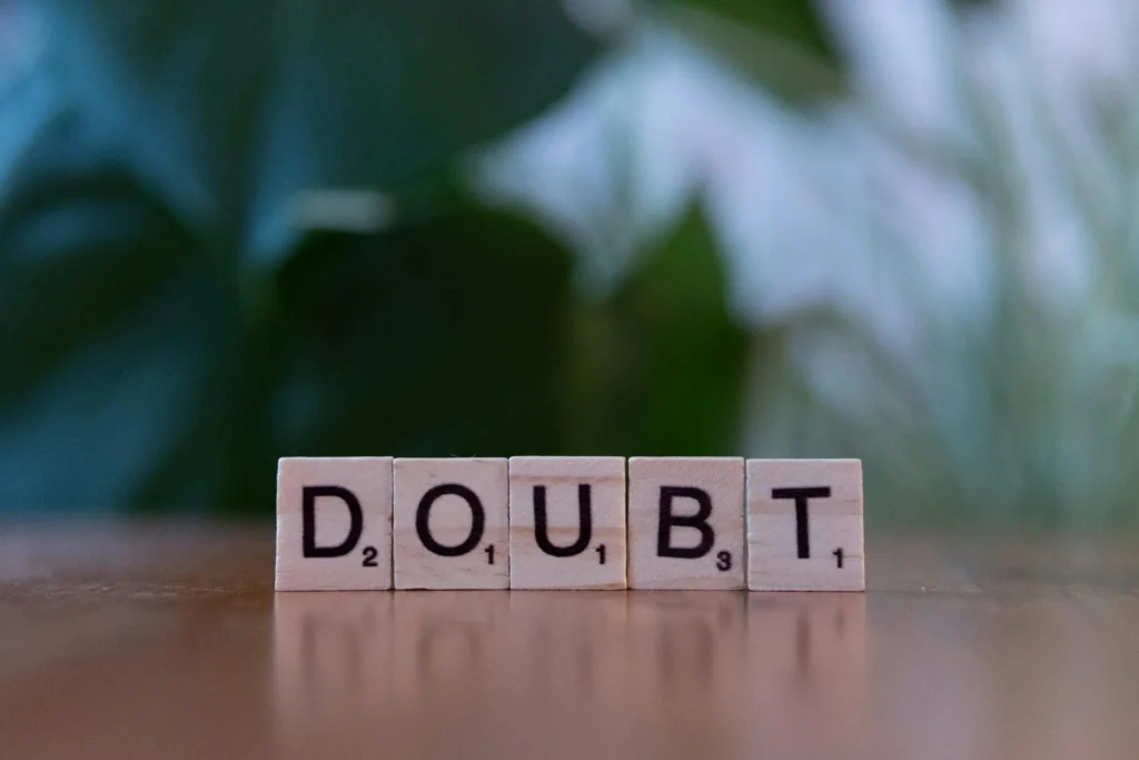 Close-up of the Spanish word ‘duda’ (doubt) formed with wooden Scrabble tiles on a surface with a blurred green background.