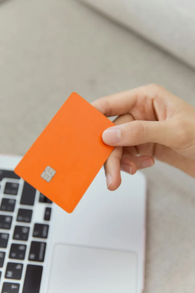 Person holding an orange chip card near a laptop keyboard.