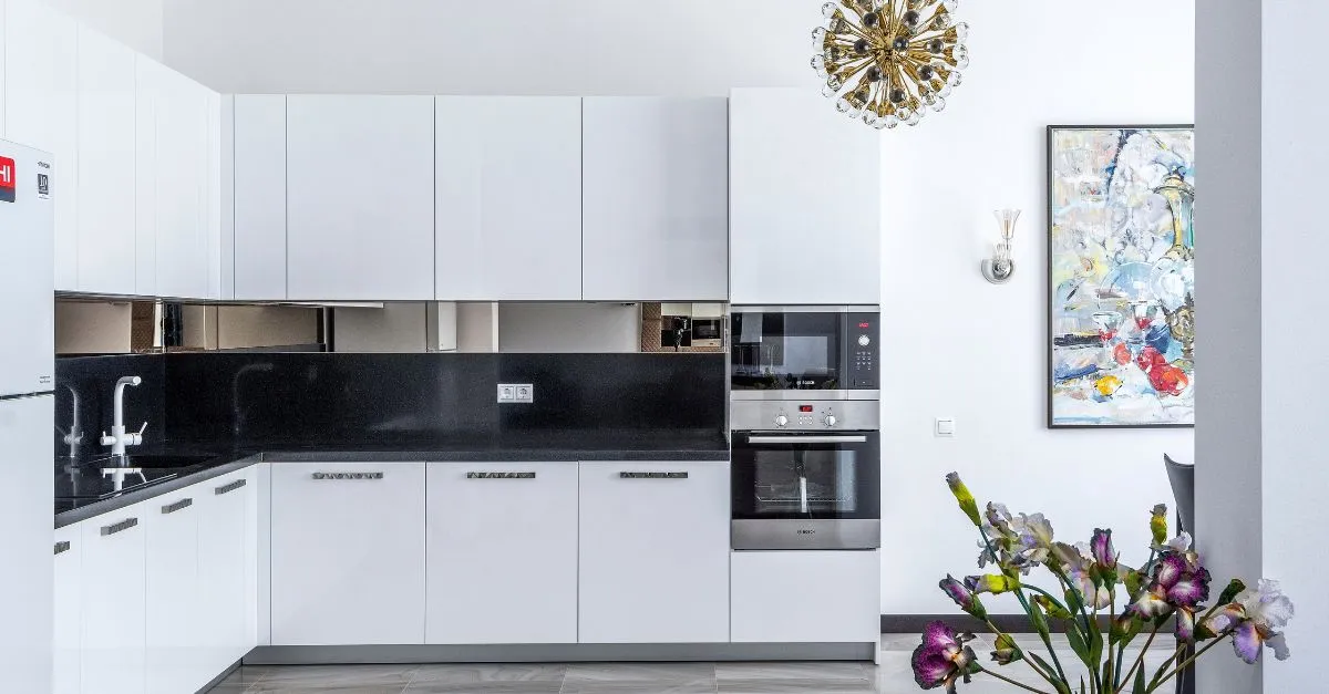 ocina blanca de estilo moderno con muebles integrados, encimera negra, horno y microondas empotrados, decorada con un cuadro colorido y un ramo de flores.