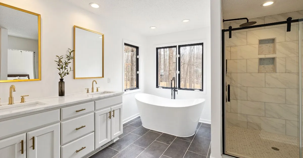 Baño amplio y luminoso con doble lavabo, bañera independiente, ducha de vidrio y acabados en tonos blancos y dorados