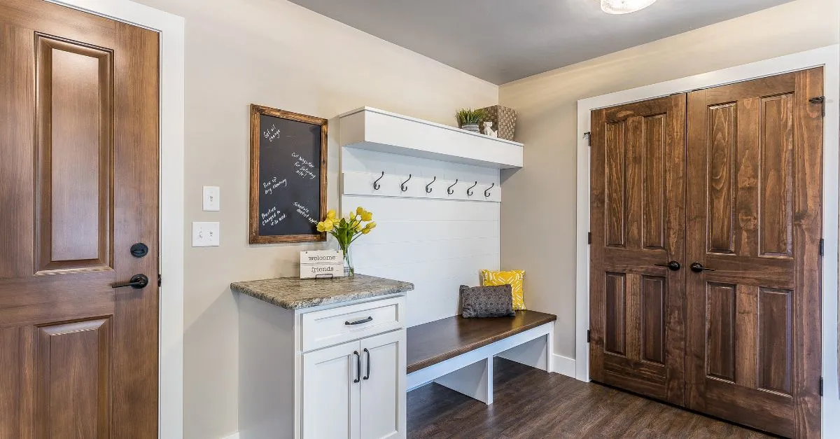 Recibidor con puerta de madera, banco con cojines, perchero con ganchos y pequeños detalles decorativos que generan una bienvenida agradable