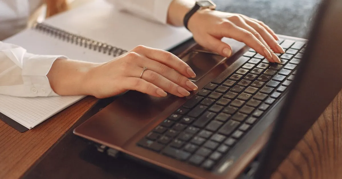 Manos de una persona escribiendo en un ordenador portátil junto a una libreta, representando la sencillez de la plataforma online de Apartur para denunciar alojamientos turísticos ilegales