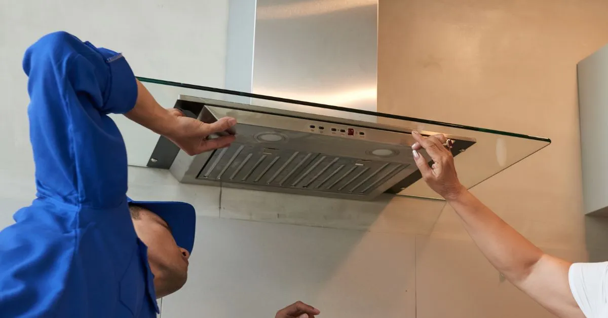 Two people checking and installing a stainless steel kitchen extractor hood in a home.