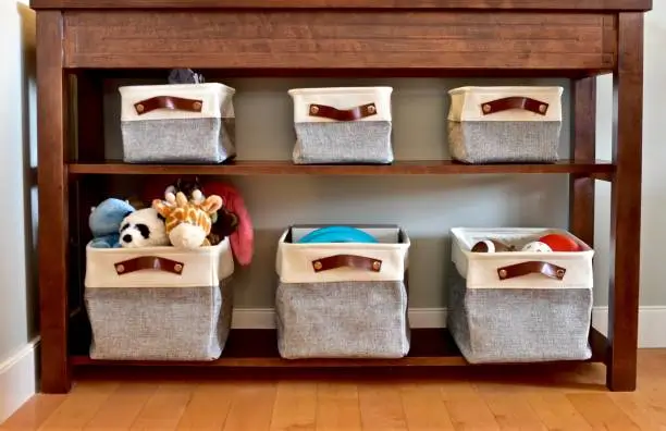 Wooden shelving unit with five fabric storage baskets, some filled with stuffed animals, balls, and children’s toys, perfect for keeping the home organized.