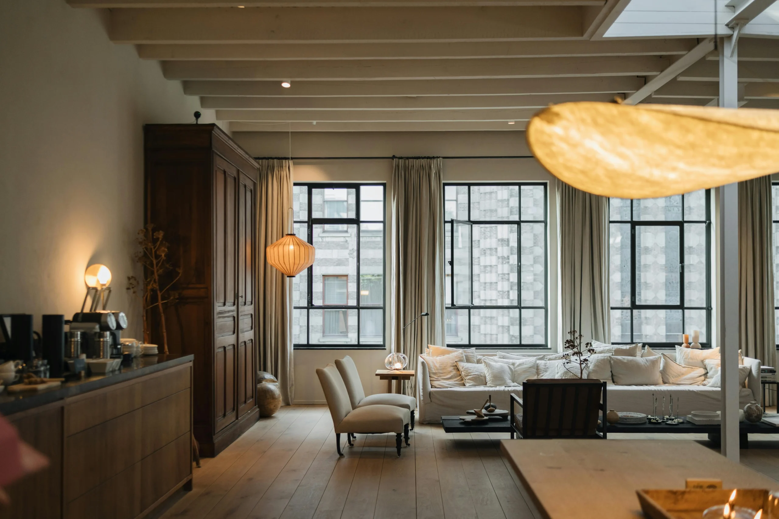 View of a living room with white sofas, warm-light lamps, and large windows that add spaciousness and comfort to the space.