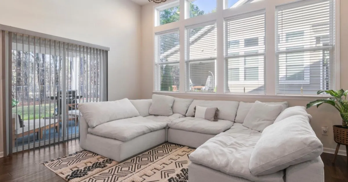 Salón con un sofá grande en forma de L, ventanales amplios con luz natural y decoración minimalista