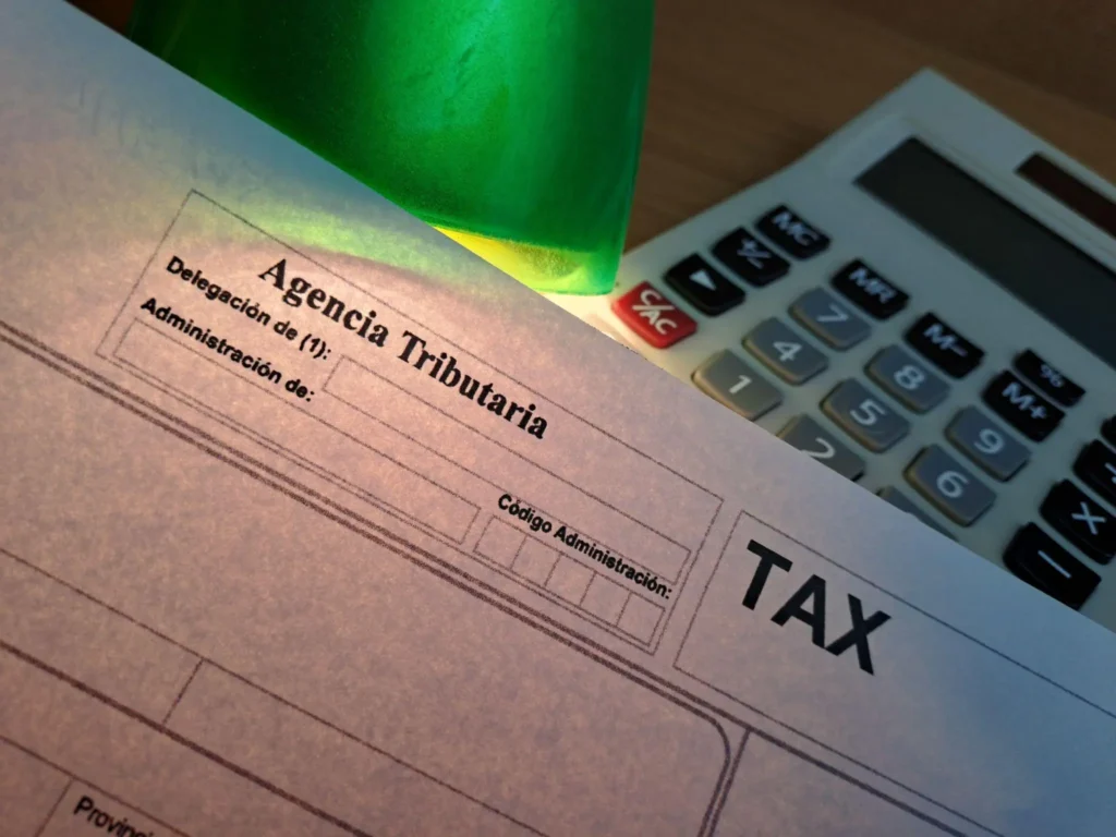 Detall d’un formulari de l’Agència Tributària sobre una taula de treball, amb una calculadora i material d’oficina, relacionat amb tràmits fiscals i administratius