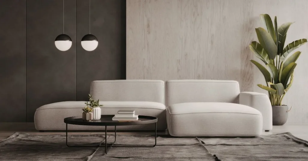 Vista d’un saló modern amb un sofà gris clar, una taula de centre negra, dues làmpades penjants i una planta decorativa a la cantonada. El disseny minimalista destaca la senzillesa i l’elegància de l’espai.