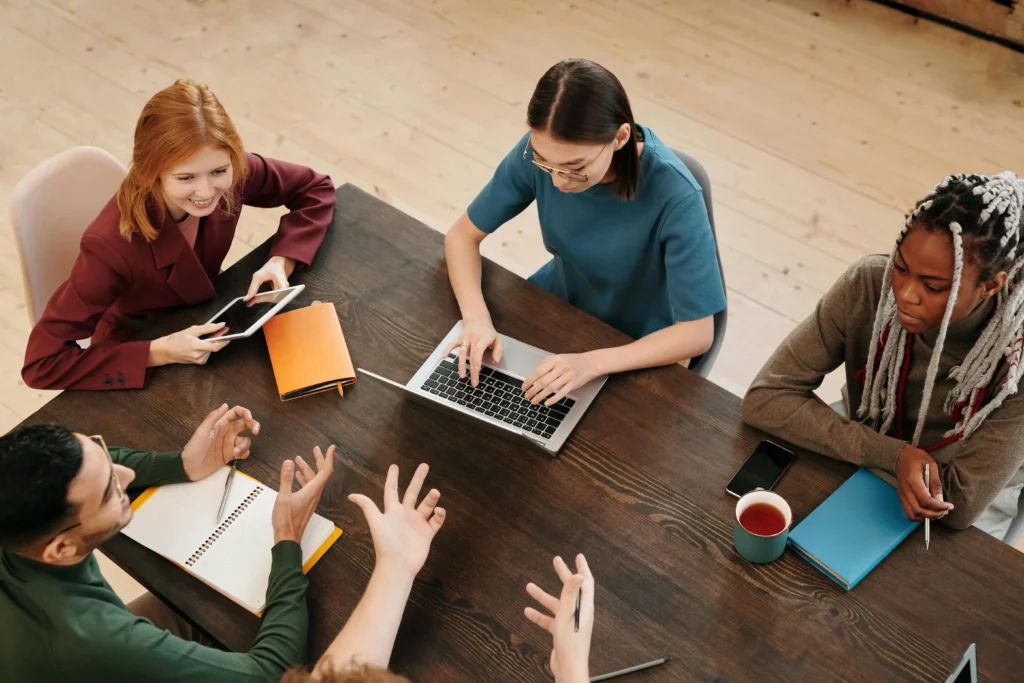 Grupo de profesionales reunidos alrededor de una mesa durante una sesión de trabajo colaborativa, utilizando un ordenador portátil, una tablet y material de oficina.