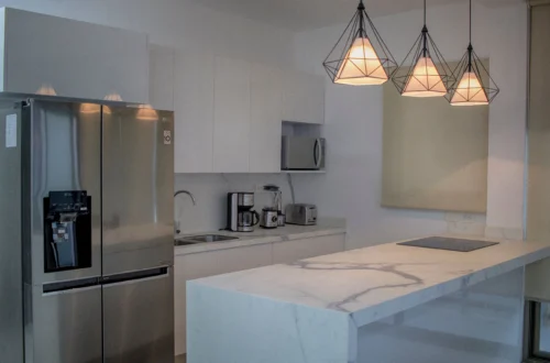 Modern apartment kitchen with a marble island, stainless steel fridge and contemporary pendant lights.