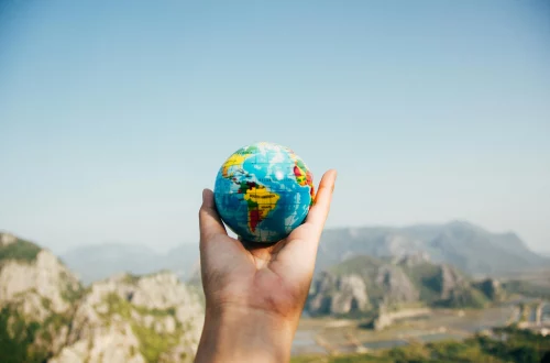 Una mano sosteniendo un globo terráqueo en un paisaje montañoso, representando el impacto global del turismo responsable y la importancia de viajar de manera consciente para proteger el planeta