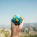 Una mano sosteniendo un globo terráqueo en un paisaje montañoso, representando el impacto global del turismo responsable y la importancia de viajar de manera consciente para proteger el planeta