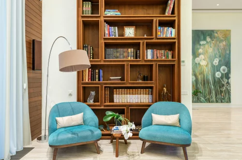 Rincón de lectura con dos sillones turquesa, lámpara de pie y una estantería de madera repleta de libros y adornos.