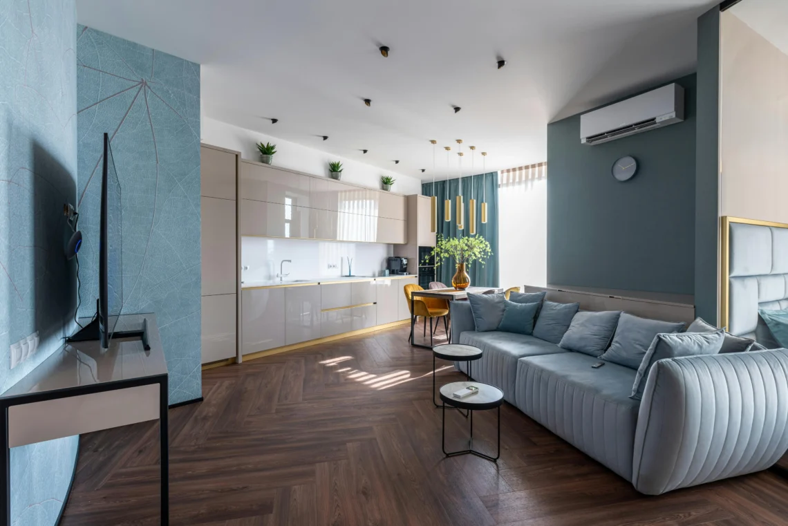 Contemporary living room with light blue sofa, open kitchen with glossy cabinets, and dining area with mustard chairs, in an elegant apartment in Barcelona.