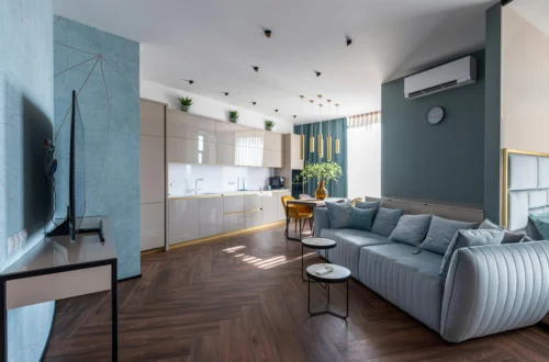 Contemporary living room with light blue sofa, open kitchen with glossy cabinets, and dining area with mustard chairs, in an elegant apartment in Barcelona.