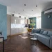 Contemporary living room with light blue sofa, open kitchen with glossy cabinets, and dining area with mustard chairs, in an elegant apartment in Barcelona.