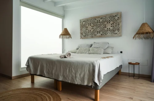 Minimalist bedroom with neutral tones and natural textures, featuring hanging wicker lamps, macramé cushions, and a wooden side table.